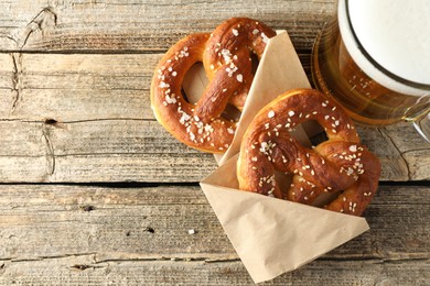 Photo of Tasty pretzels and glass of beer on wooden table, flat lay. Space for text