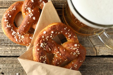 Photo of Tasty pretzels and glass of beer on wooden table, flat lay