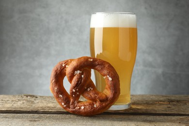 Photo of Tasty pretzel and glass of beer on wooden table against grey background, closeup