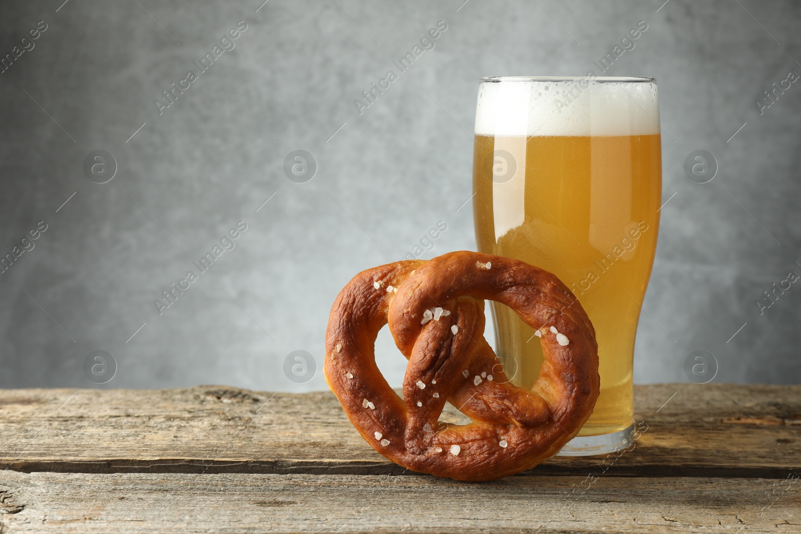 Tasty pretzel and glass of beer on wooden table against grey background, closeup. Space for text Photo of Tasty pretzel and glass of beer on wooden table against grey background, closeup. Space for text