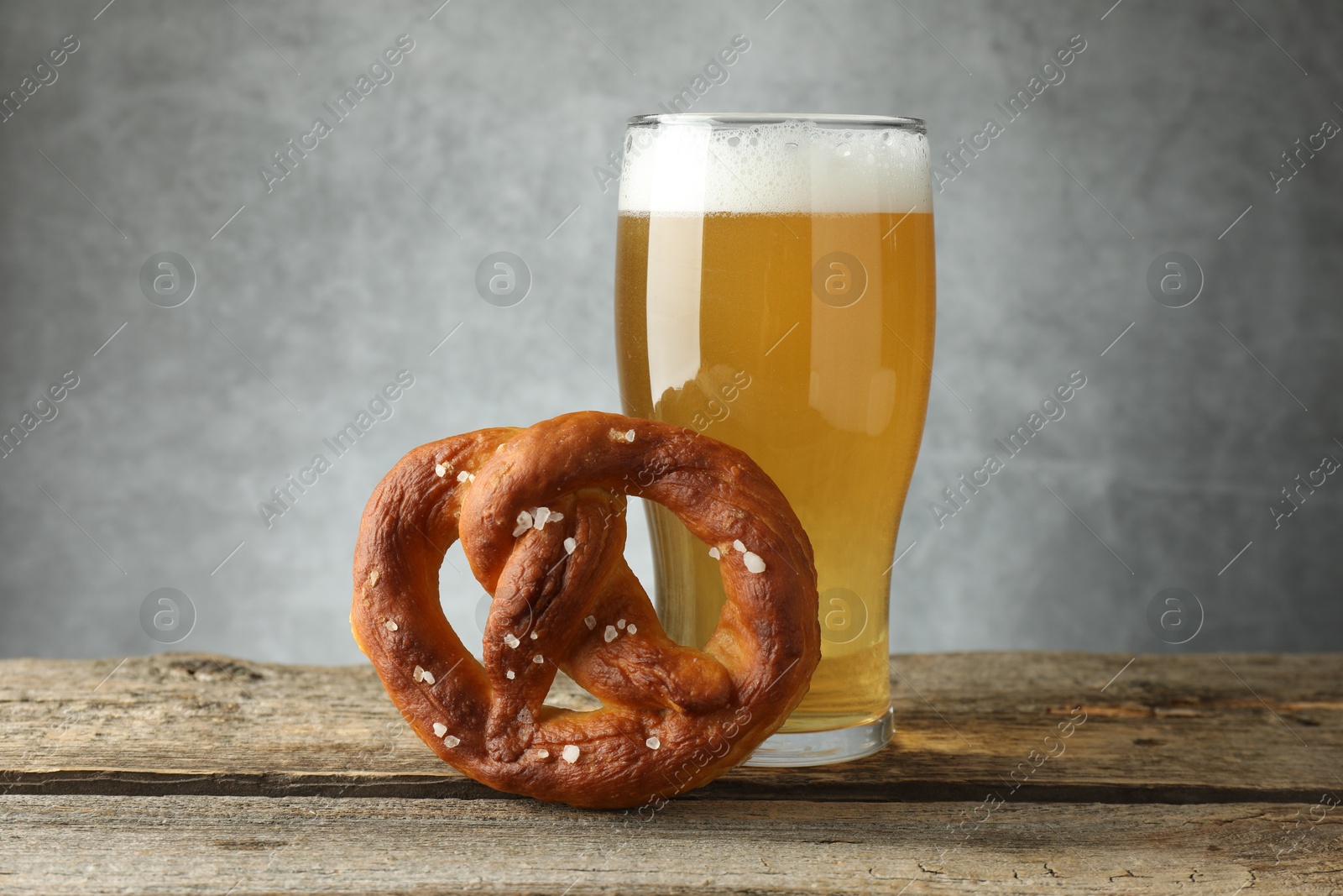 Tasty pretzel and glass of beer on wooden table against grey background, closeup Photo of Tasty pretzel and glass of beer on wooden table against grey background, closeup