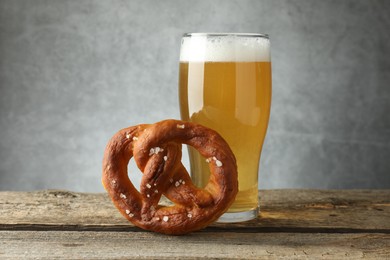 Photo of Tasty pretzel and glass of beer on wooden table against grey background, closeup