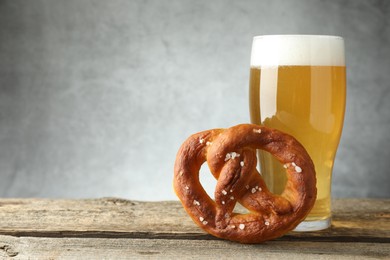 Photo of Tasty pretzel and glass of beer on wooden table against grey background, closeup. Space for text