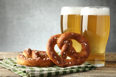 Photo of Tasty pretzels and glasses of beer on wooden table against grey background, closeup
