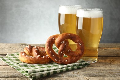 Photo of Tasty pretzels and glasses of beer on wooden table against grey background, closeup