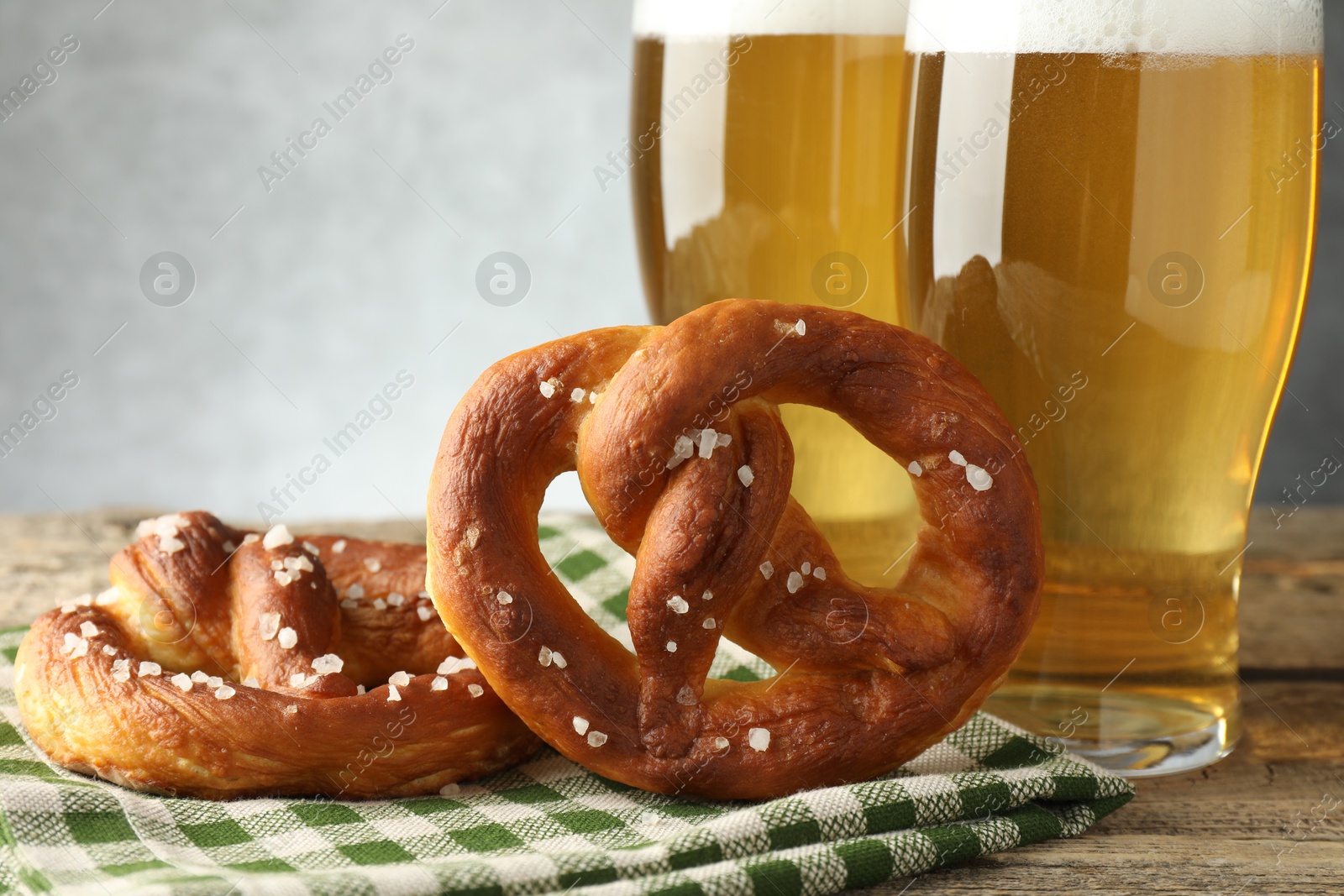 Photo of Tasty pretzels and glasses of beer on wooden table against grey background, closeup