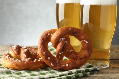 Photo of Tasty pretzels and glasses of beer on wooden table against grey background, closeup