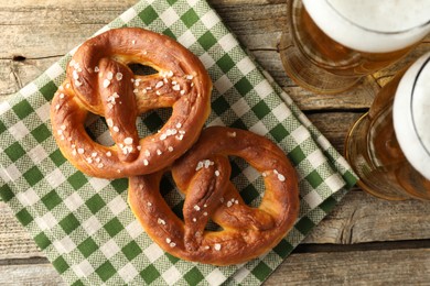 Photo of Tasty pretzels and glasses of beer on wooden table, flat lay