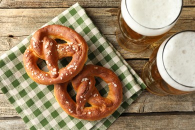 Photo of Tasty pretzels and glasses of beer on wooden table, flat lay