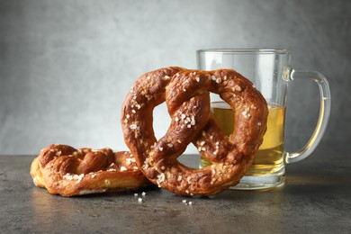 Photo of Tasty pretzels and glass of beer on dark textured table against grey background, closeup