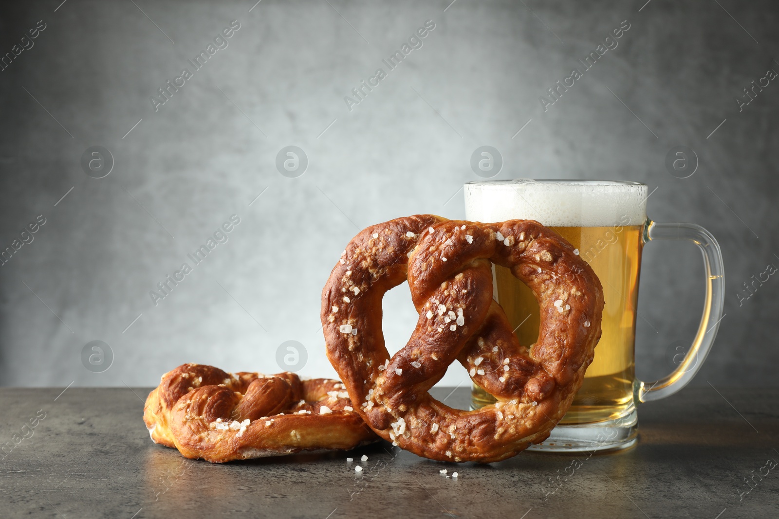 Tasty pretzels and glass of beer on dark textured table against grey background, closeup Photo of Tasty pretzels and glass of beer on dark textured table against grey background, closeup