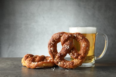 Photo of Tasty pretzels and glass of beer on dark textured table against grey background, closeup