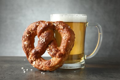 Photo of Tasty pretzel and glass of beer on dark textured table against grey background, closeup