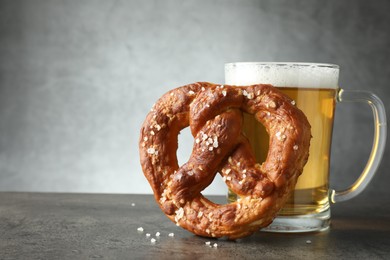 Photo of Tasty pretzel and glass of beer on dark textured table against grey background, closeup. Space for text