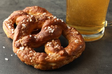 Photo of Tasty pretzels and glass of beer on dark textured table, closeup