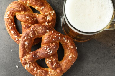 Photo of Tasty pretzels and glass of beer on dark textured table, flat lay