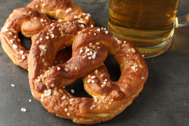Photo of Tasty pretzels and glass of beer on dark textured table, closeup