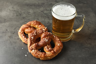 Photo of Tasty pretzels and glass of beer on dark textured table, closeup