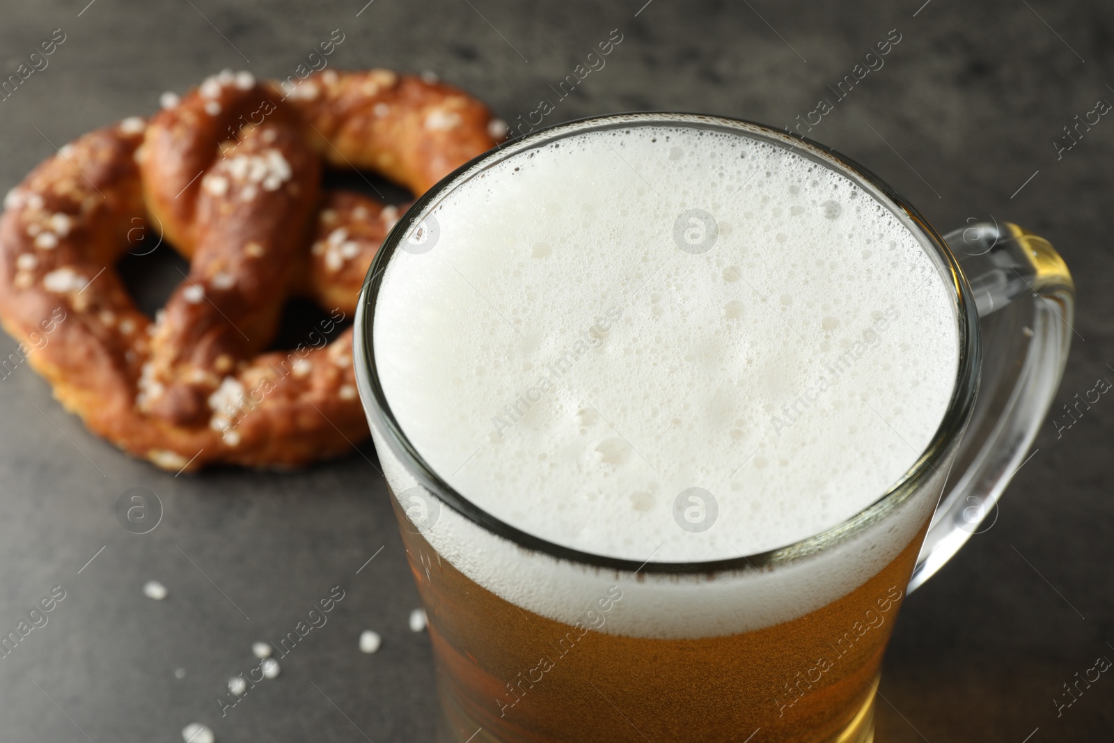 Glass of beer and tasty pretzel on dark textured table, selective focus Photo of Glass of beer and tasty pretzel on dark textured table, selective focus