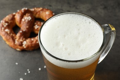 Photo of Glass of beer and tasty pretzel on dark textured table, selective focus
