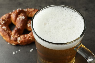 Photo of Glass of beer and tasty pretzel on dark textured table, selective focus
