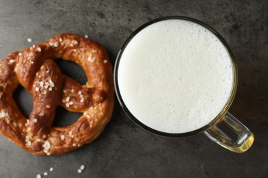Photo of Tasty pretzel and glass of beer on dark textured table, flat lay