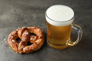 Photo of Tasty pretzel and glass of beer on dark textured table, closeup