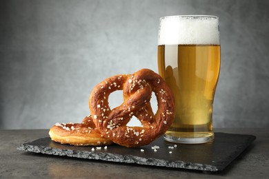 Photo of Tasty pretzels and glass of beer on dark textured table against grey background, closeup