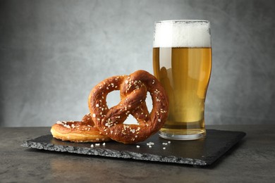 Photo of Tasty pretzels and glass of beer on dark textured table against grey background, closeup