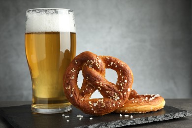 Photo of Tasty pretzels and glass of beer on dark textured table against grey background, closeup