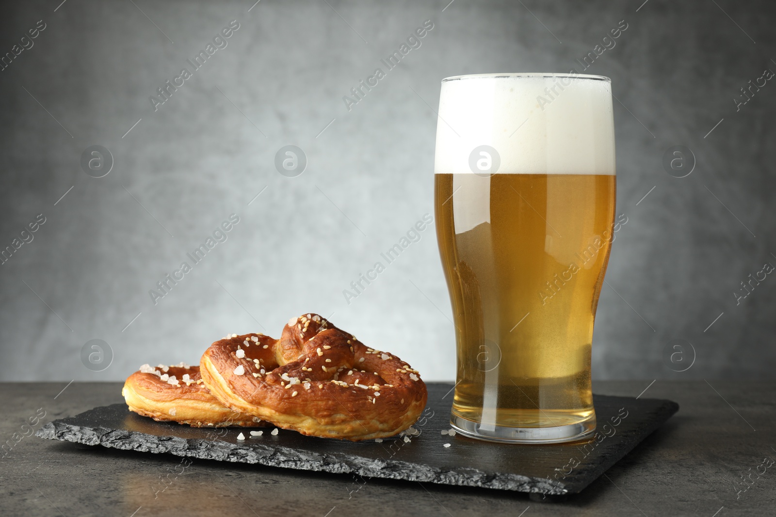 Tasty pretzels and glass of beer on dark textured table against grey background, closeup Photo of Tasty pretzels and glass of beer on dark textured table against grey background, closeup