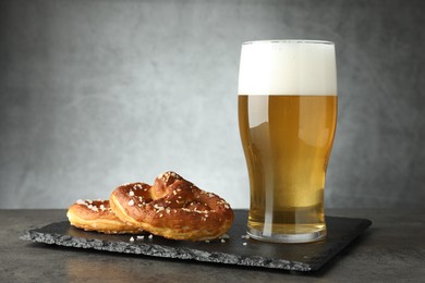 Photo of Tasty pretzels and glass of beer on dark textured table against grey background, closeup