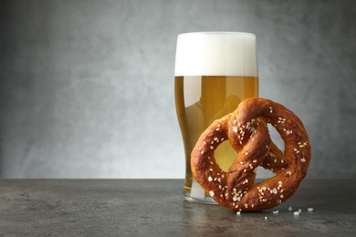 Photo of Tasty pretzel and glass of beer on dark textured table against grey background, closeup. Space for text