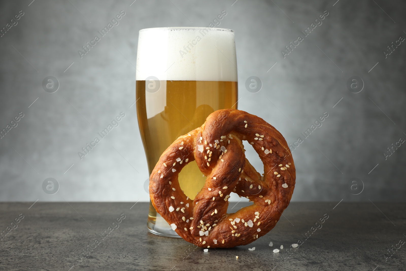 Tasty pretzel and glass of beer on dark textured table against grey background, closeup Photo of Tasty pretzel and glass of beer on dark textured table against grey background, closeup