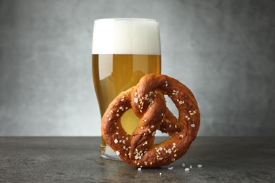 Photo of Tasty pretzel and glass of beer on dark textured table against grey background, closeup