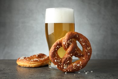 Photo of Tasty pretzels and glass of beer on dark textured table against grey background, closeup