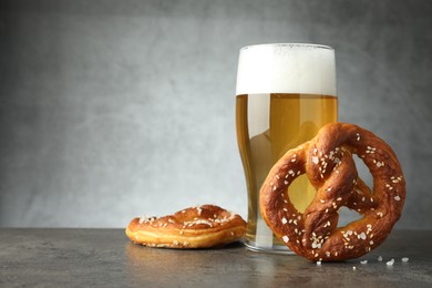 Photo of Tasty pretzels and glass of beer on dark textured table against grey background, closeup. Space for text