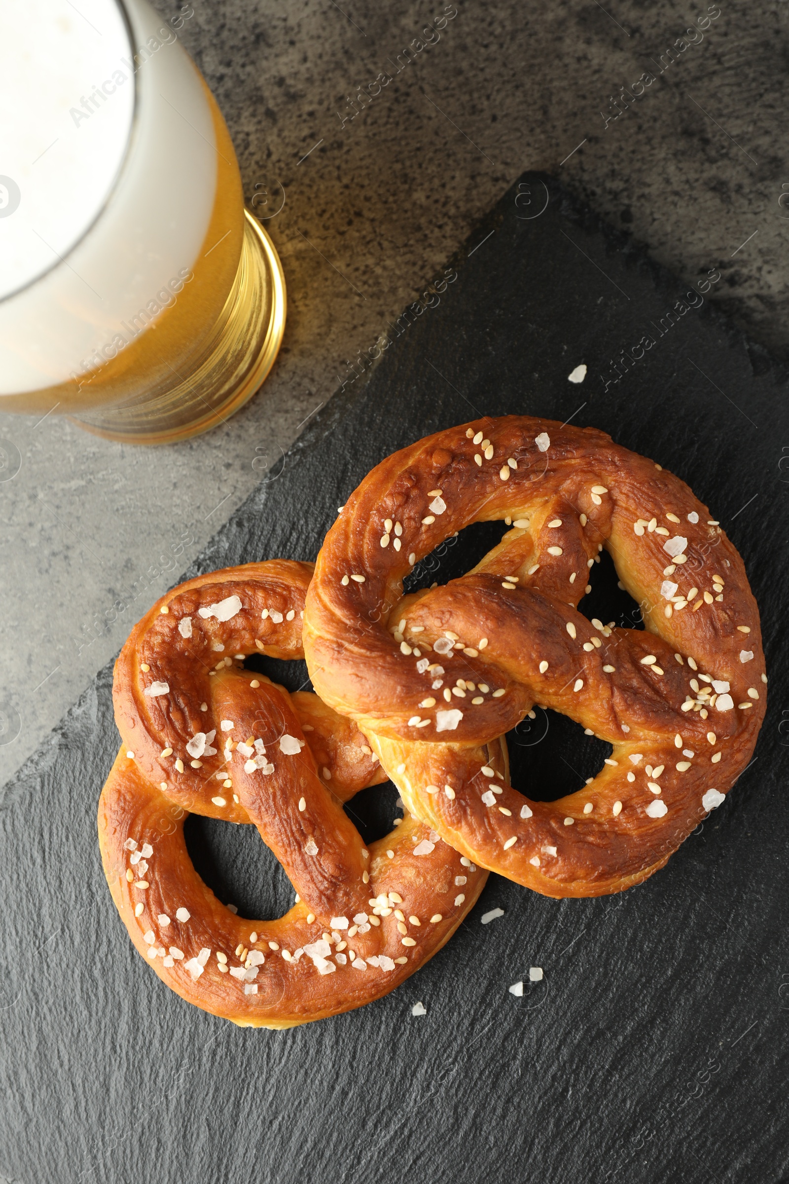 Tasty pretzels and glass of beer on dark textured table, flat lay Photo of Tasty pretzels and glass of beer on dark textured table, flat lay