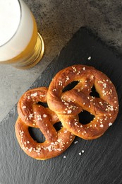 Photo of Tasty pretzels and glass of beer on dark textured table, flat lay