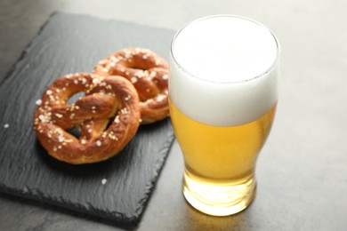 Photo of Tasty pretzels and glass of beer on dark textured table, closeup
