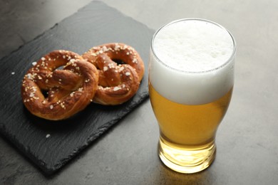 Photo of Tasty pretzels and glass of beer on dark textured table, closeup