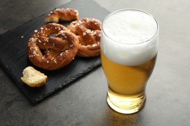 Photo of Tasty pretzels and glass of beer on dark textured table, closeup