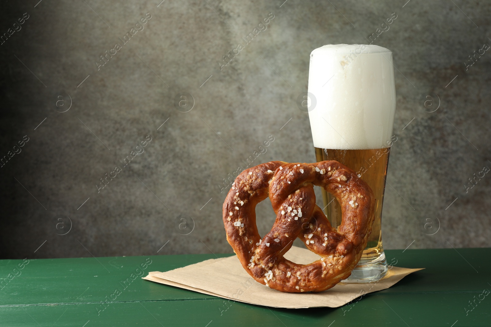 Tasty pretzel and glass of beer on green wooden table against grey textured background, closeup. Space for text Photo of Tasty pretzel and glass of beer on green wooden table against grey textured background, closeup. Space for text