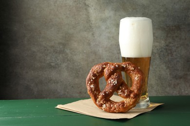 Photo of Tasty pretzel and glass of beer on green wooden table against grey textured background, closeup. Space for text
