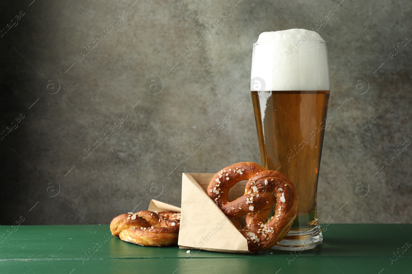 Tasty pretzels and glass of beer on green wooden table against grey textured background, closeup. Space for text Photo of Tasty pretzels and glass of beer on green wooden table against grey textured background, closeup. Space for text