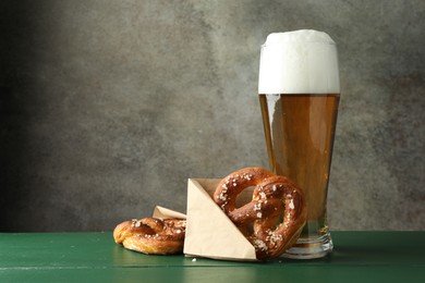 Photo of Tasty pretzels and glass of beer on green wooden table against grey textured background, closeup. Space for text