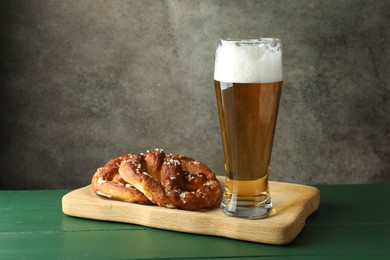 Photo of Tasty pretzels and glass of beer on green wooden table against grey textured background, closeup