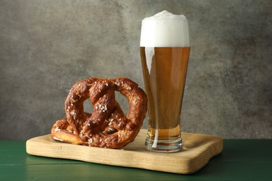 Photo of Tasty pretzels and glass of beer on green wooden table against grey textured background, closeup
