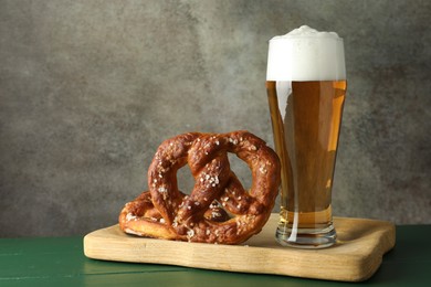 Photo of Tasty pretzels and glass of beer on green wooden table against grey textured background, closeup
