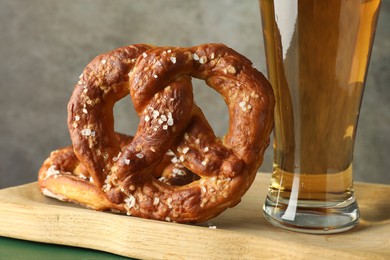 Photo of Tasty pretzels and glass of beer on green wooden table against grey background, closeup